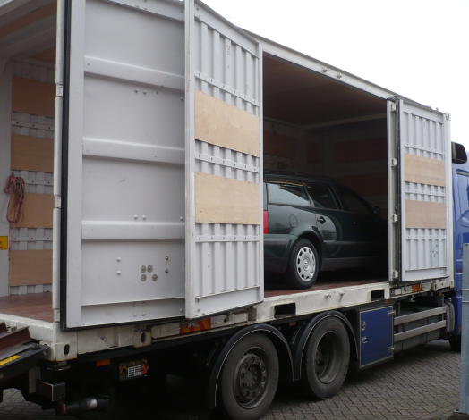 Afbeelding van een auto die in een container staat achterop een vrachtwagen.