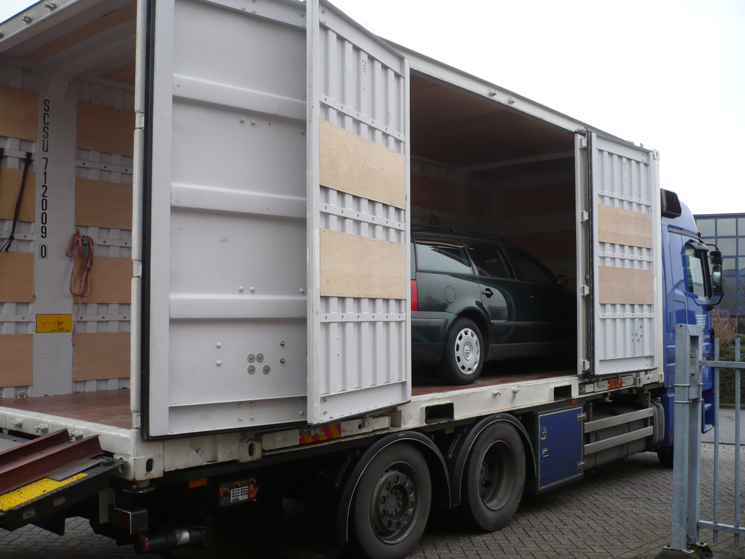 Afbeelding van een auto die in een container staat achterop een vrachtwagen.