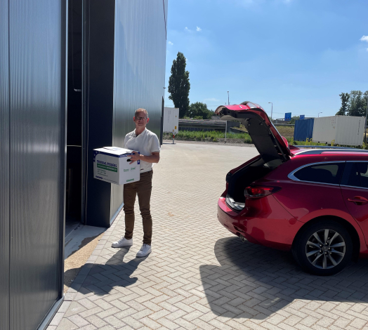 Afbeelding van directeur Lauwrens de Jong met een verhuisdoos voor de ingang van het opslagpand.